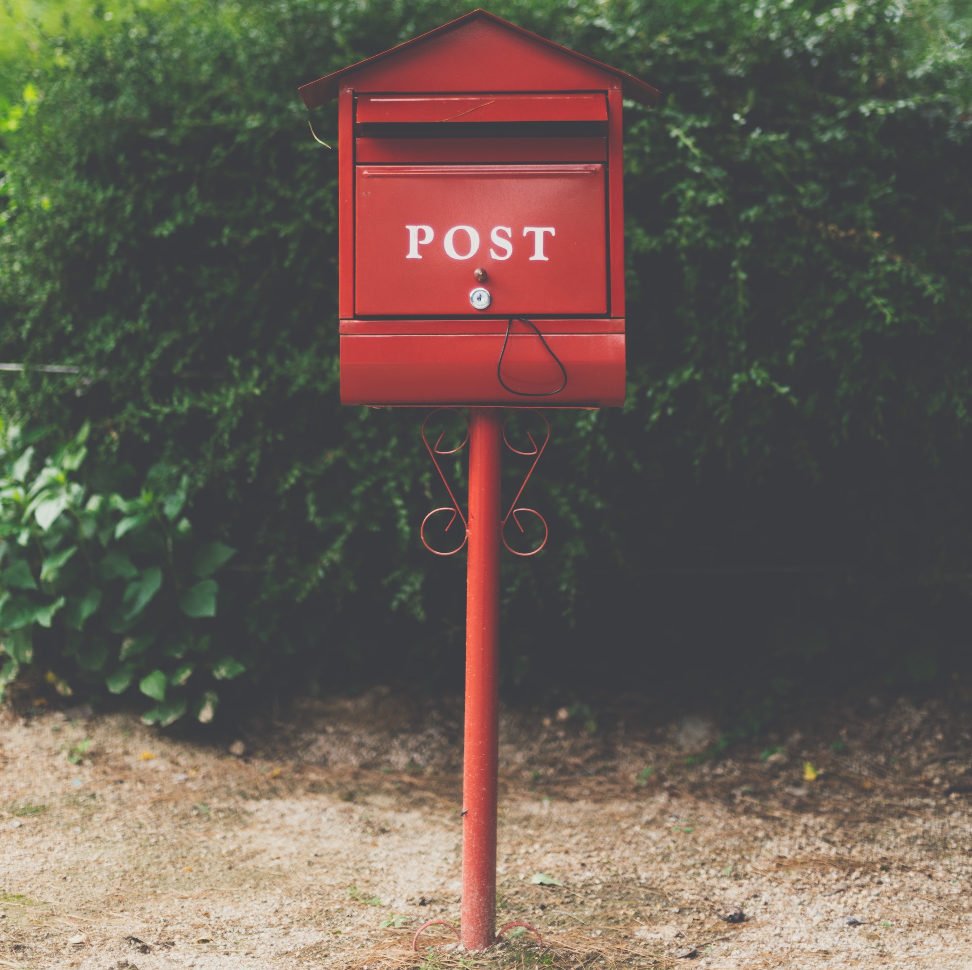 Mailbox with 'post' written on the front, greenery in the background